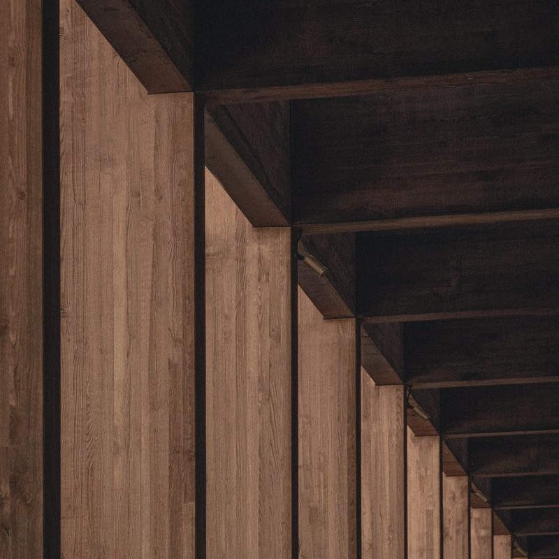 A timber colonnade with exposed roof beams casting deep shade